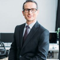 smiling-businessman-in-eyeglasses-sitting-on-table-in-office-3.jpeg